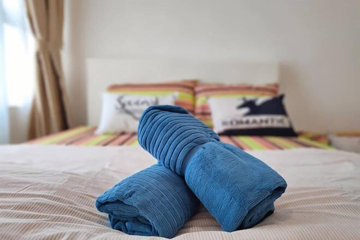 A neatly made bed with a folded blue towel, striped bedding, and pillows with text.