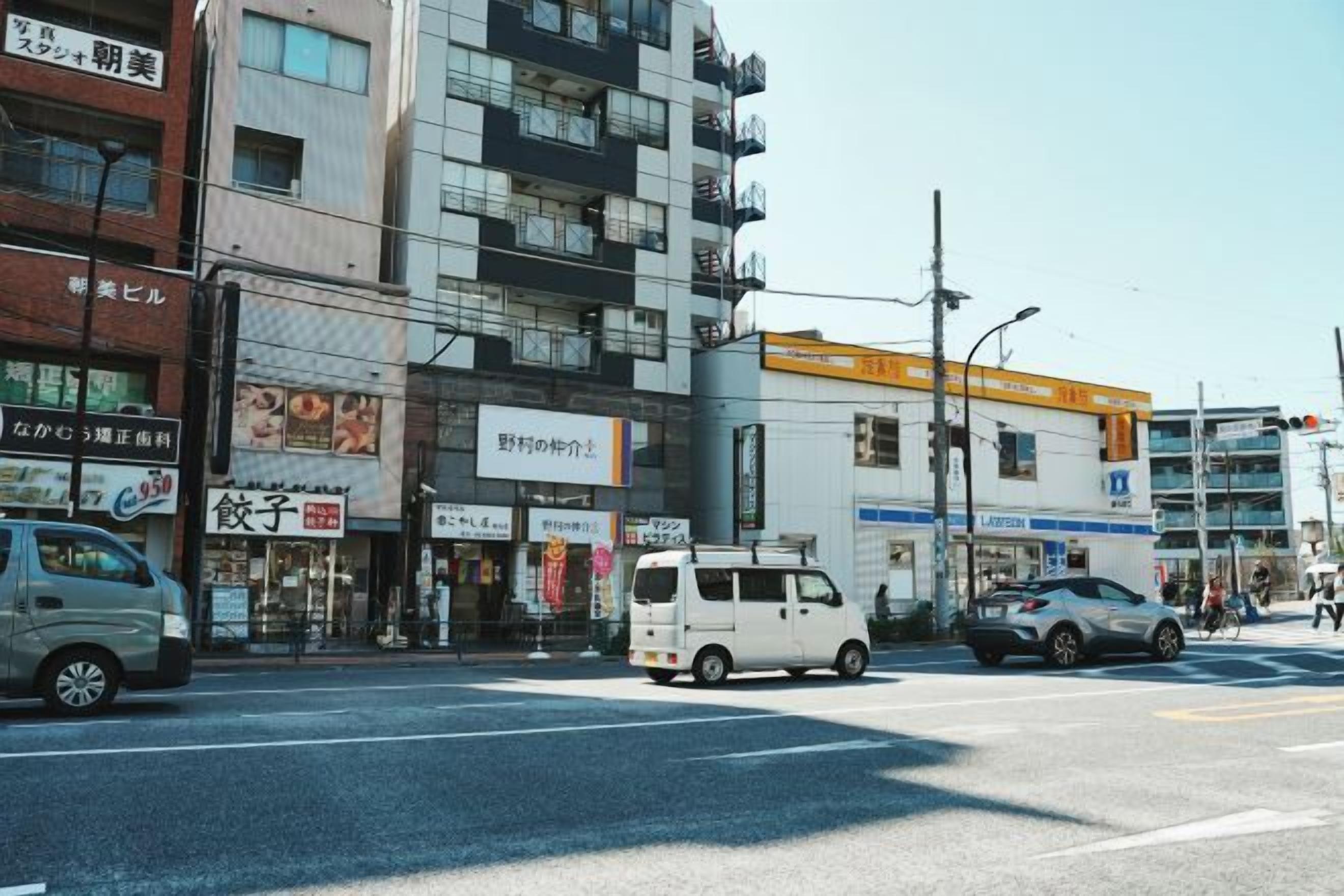 A street view with a white van and a car, buildings with various signs, and a clear sky.