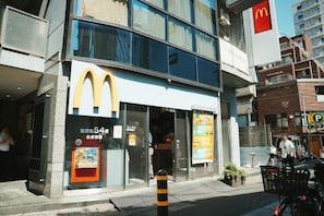 Un restaurant McDonald's avec une façade en verre transparent, une entrée bien visible et un panneau indiquant le parking en arrière-plan.