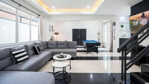 A modern living room with a grey sofa, a pool table, and a TV. - White Chocolate Pool Villa (Bang Lamung)