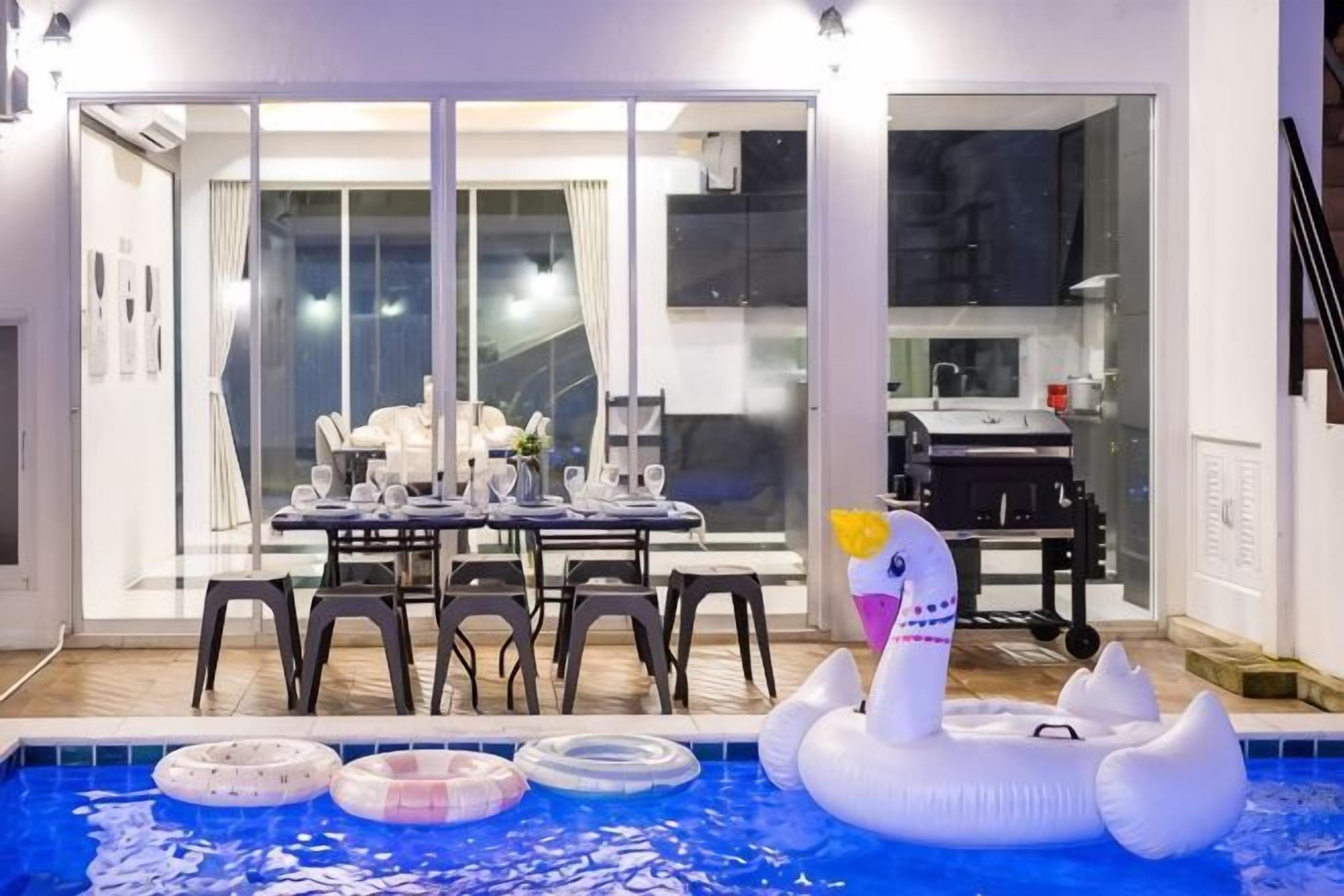 An indoor swimming pool with inflatable toys, a dining area with a table and chairs, and a view through glass doors.