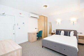 Habitación de hotel con cama, escritorio, silla, armario y dos luces fijadas a la pared.