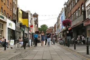 Calle peatonal bordeada de tiendas y cafés, con gente caminando y sentada en terrazas.