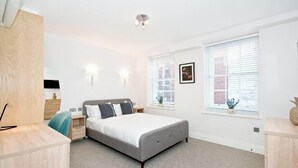 A bedroom with a bed, bedside tables, a desk, a chair, and a window with blinds.