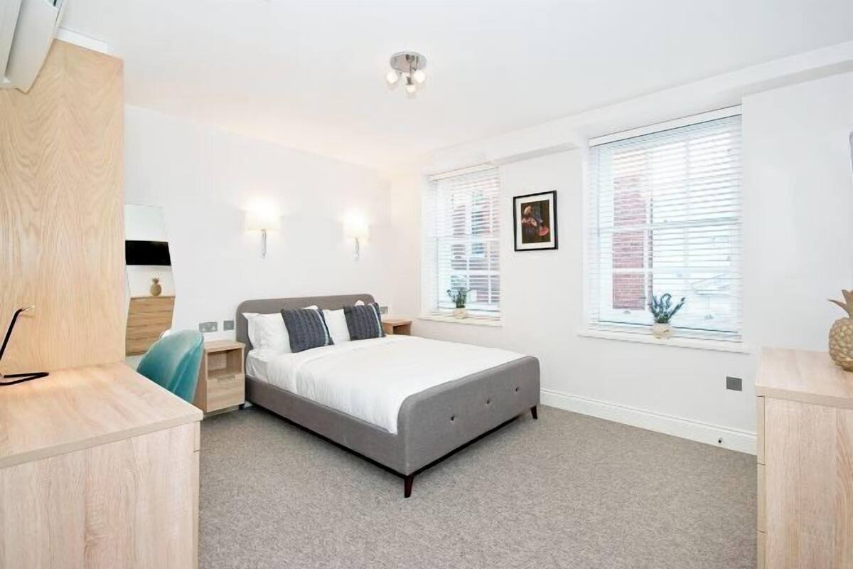 Une chambre à coucher comprenant un lit, des tables de chevet, un bureau, une chaise et une fenêtre avec des stores.