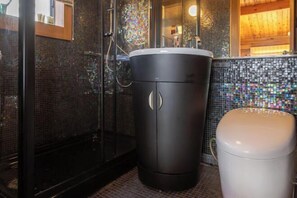A bathroom with a black cabinet, a white toilet, and a shower area with a mosaic tile wall. - SHODOSHIMA PRIVATE CAMP SITE (Shodoshima)