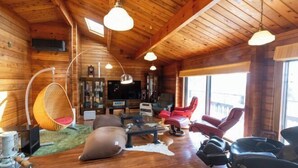 A cozy log cabin interior with a wooden floor, a large window, a television, and a comfortable seating area with a red chair and a hanging chair. - SHODOSHIMA PRIVATE CAMP SITE (Shodoshima)