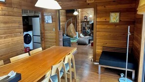 A wooden cabin interior with a dining area, a hanging chair, a sofa, and a small table with a box. - SHODOSHIMA PRIVATE CAMP SITE (Shodoshima)