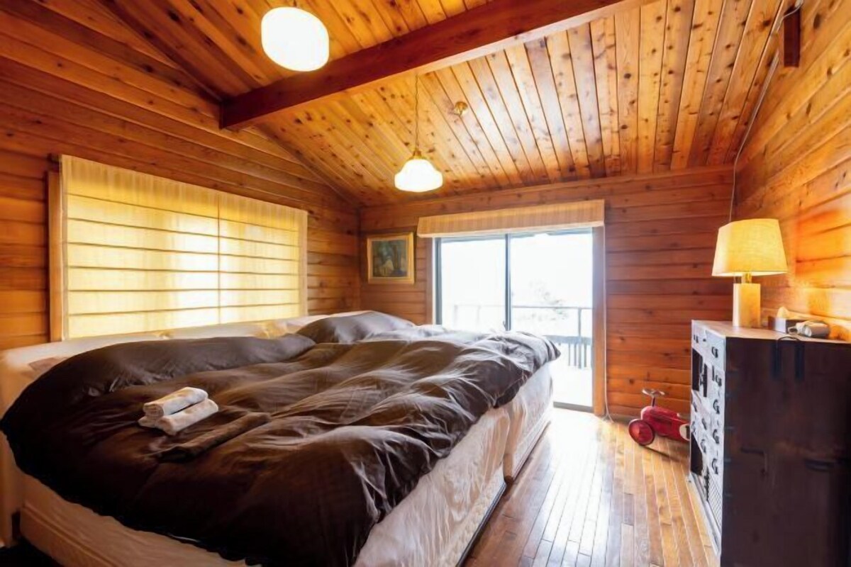 A wooden cabin room with a bed, a dresser, and a window.