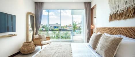 A modern hotel room with a large bed, a view of the outdoors, a television, and a woven basket.