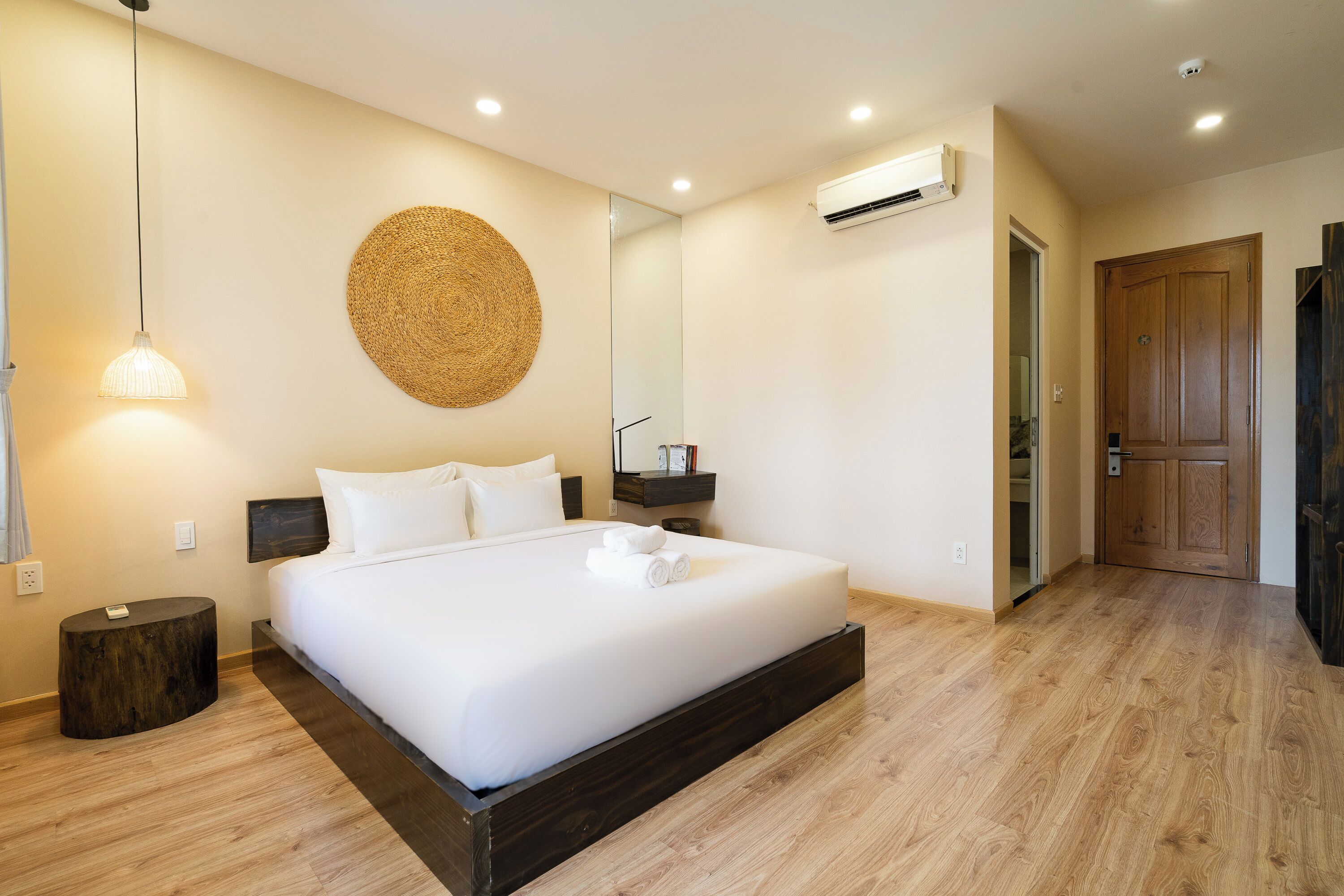 A bedroom with a bed, bedside table, wall-mounted mirror, and a round woven wall decoration.