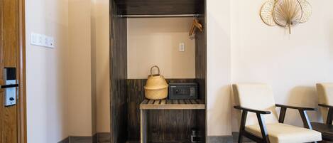 A compact room with a wooden wardrobe, a shelf with a woven basket and a radio, a pair of slippers, and two chairs.