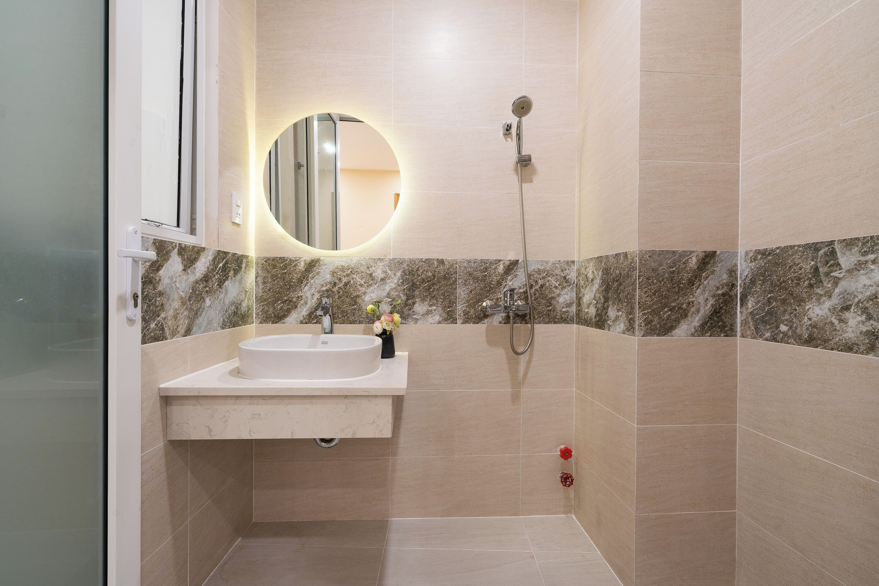 A bathroom with a sink, mirror, shower, and marble tiles.