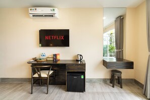 A room with a dark wooden desk, a small black refrigerator, a wall-mounted TV displaying 'NETFLIX,' and a window with curtains. - HemTouch House - Nguyen Van Mai (Xuan Hoa)