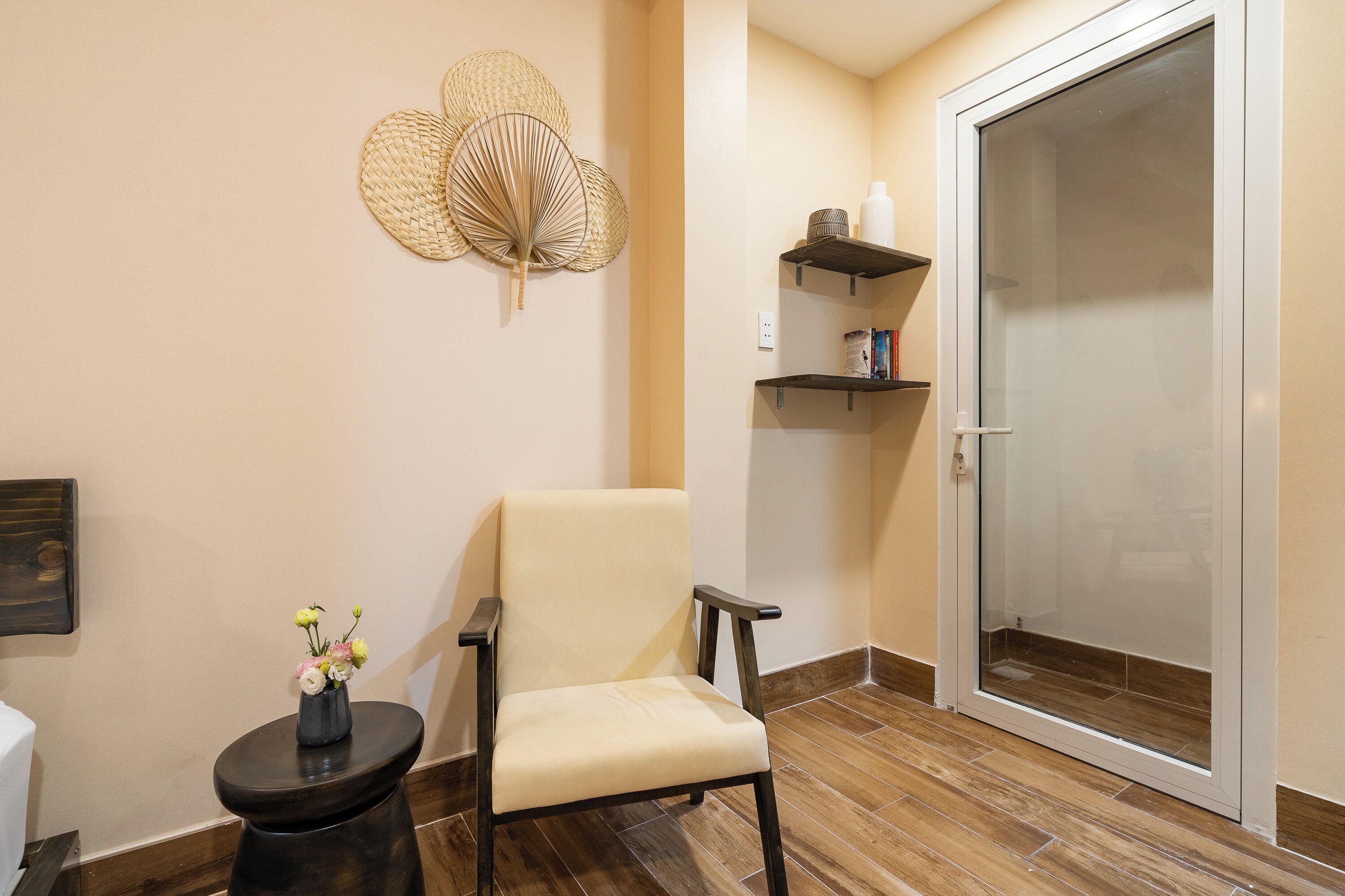 A room with a chair, a small table with a vase, a door, and shelves with items.