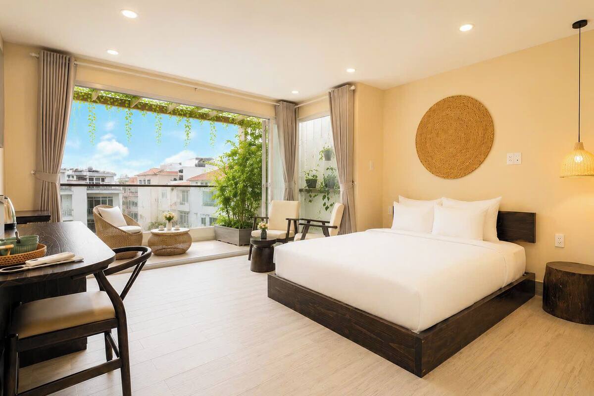 Habitación de hotel con una cama grande, un escritorio, una silla, un adorno circular tejido en la pared y vistas de edificios a través de la ventana.