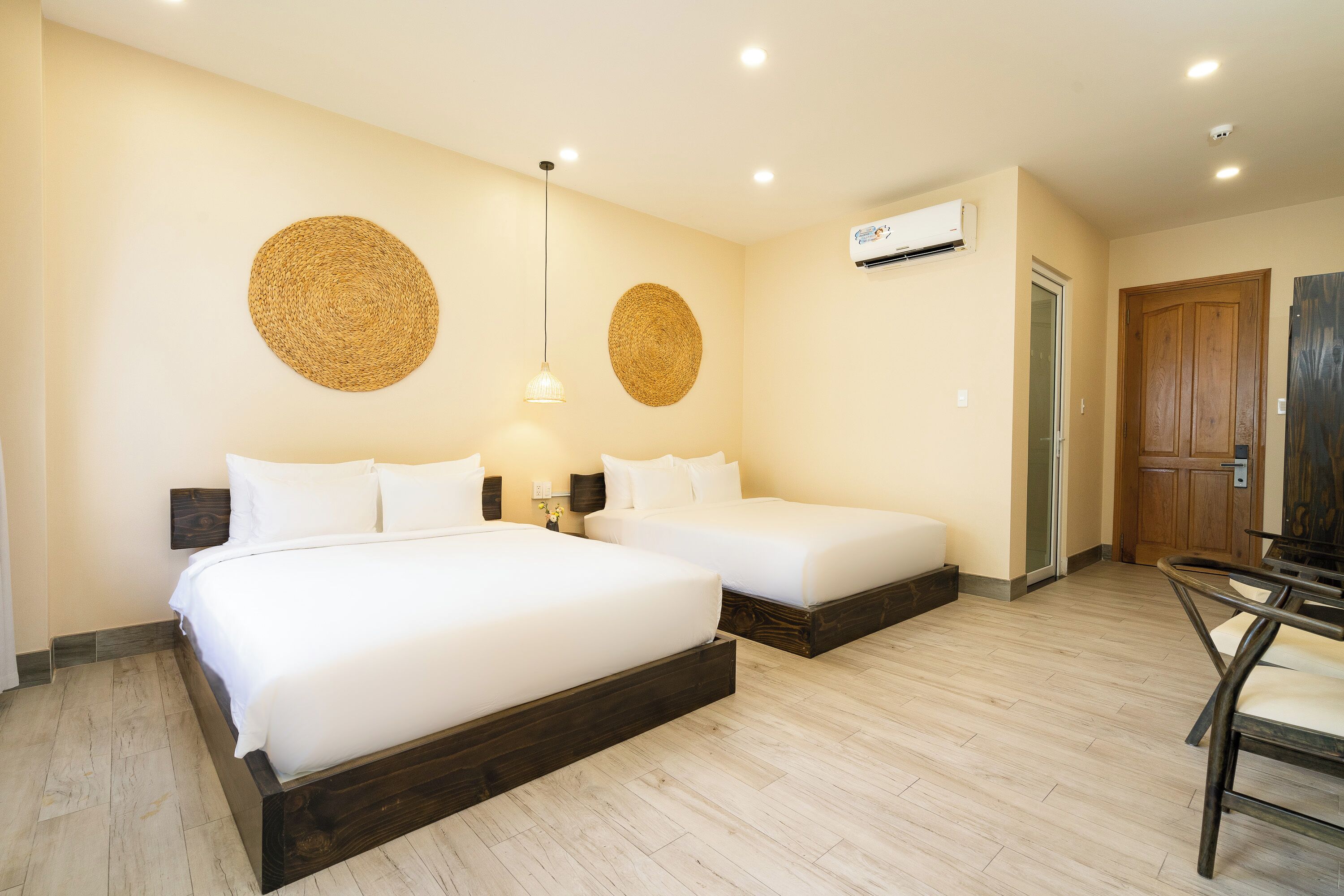 A hotel room with two beds, a wooden floor, a ceiling fan, and an air conditioning unit.