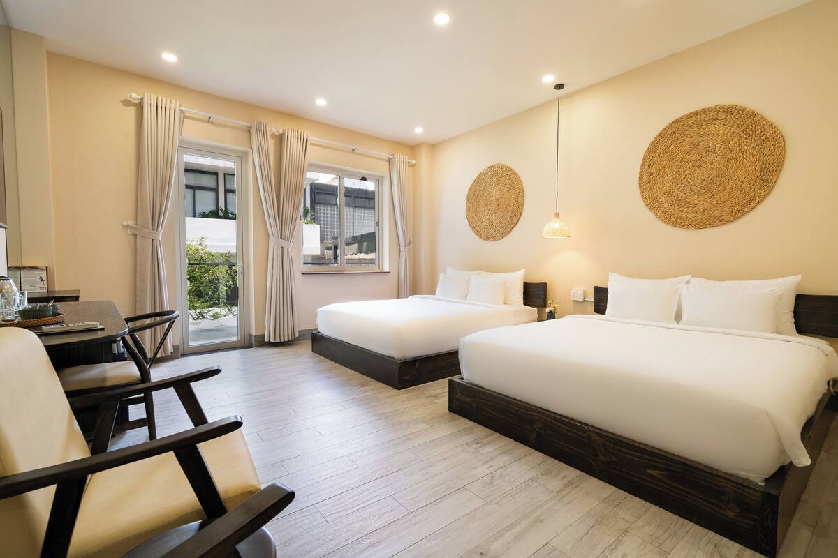 Habitación de hotel con dos camas, una mesa de comedor, sillas, una ventana con cortinas y una lámpara de pared.