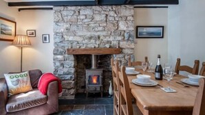 Una habitación acogedora con chimenea de piedra, una mesa de comedor para dos personas y un sofá cómodo con una manta roja.