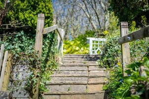 Una escalera de piedra conduce a una puerta blanca, rodeada de vegetación.