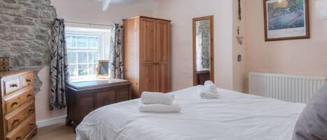 A bedroom with a bed, wooden wardrobe, stone wall, and a window with curtains.