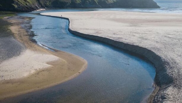 Un paisaje costero con una línea de costa curva, una playa arenosa y acantilados rocosos.