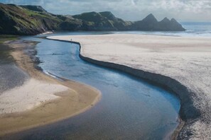 Un paisaje costero con una línea de costa curva, una playa arenosa y acantilados rocosos.