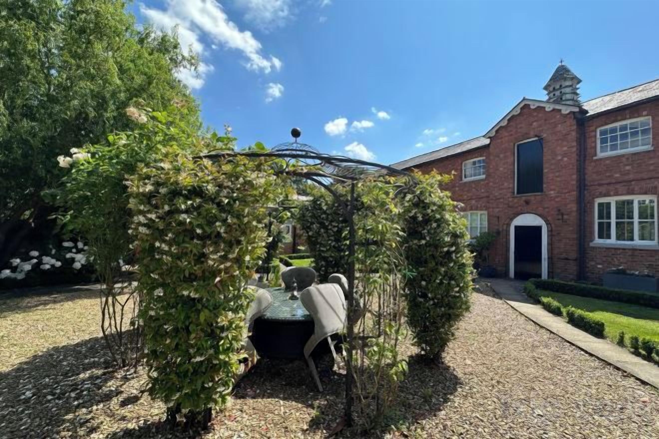 Een tuin met een prieel, een gebouw met een bakstenen gevel en een grindpad.
