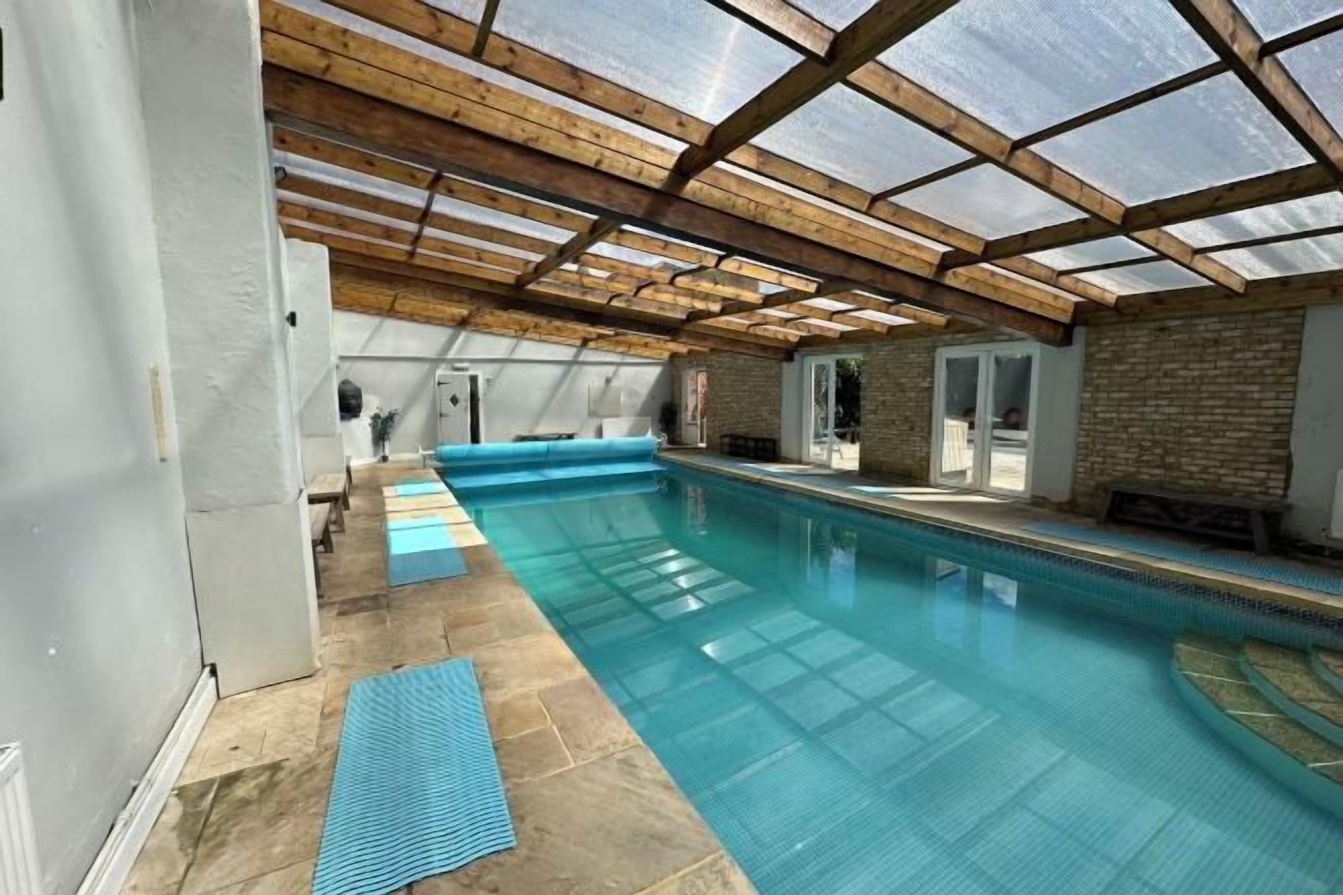 An indoor swimming pool with a glass ceiling, a brick wall, and a wooden ceiling structure.