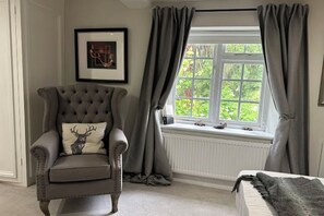 A room with a tufted armchair, a bed, a window with curtains, and a framed picture on the wall. - Huntershields (Northampton)