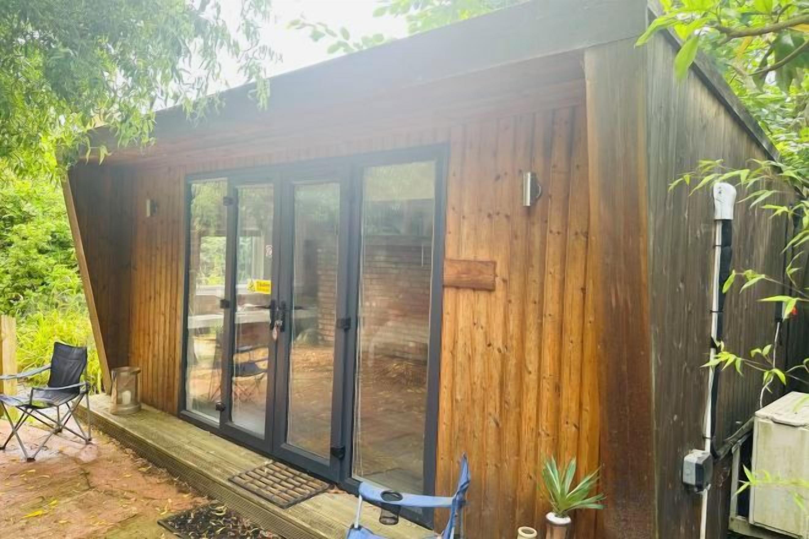 A wooden cabin with a sliding glass door entrance, a small porch area, and a potted plant.