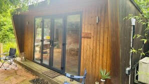 A wooden cabin with a sliding glass door entrance, a small deck, and a chair outside. - Huntershields (Northampton)