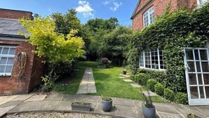 A garden with a paved pathway leading to a house with a brick facade and white windows. - Huntershields (Northampton)