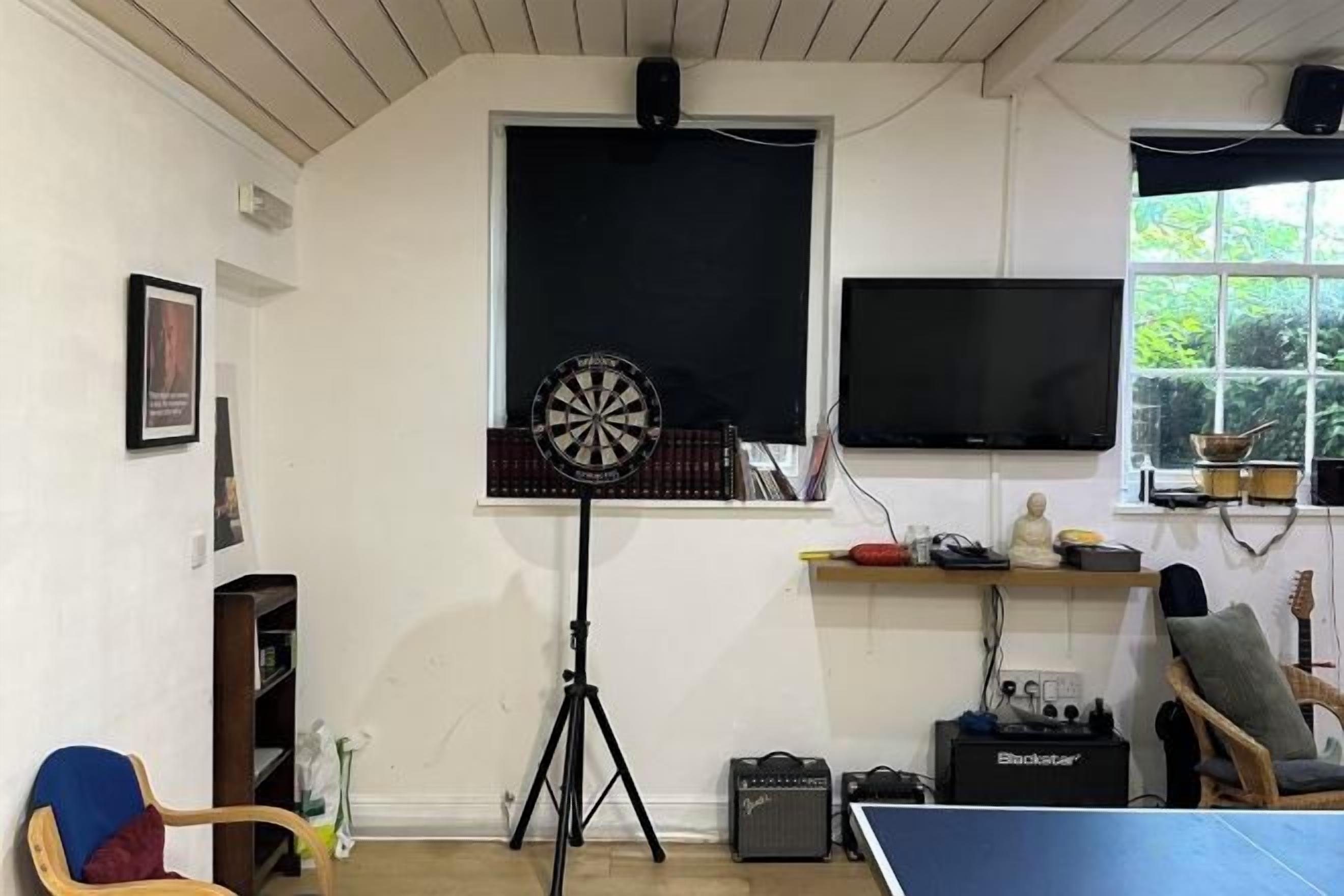 Una habitación con dardos, televisión, ventana y una guitarra.