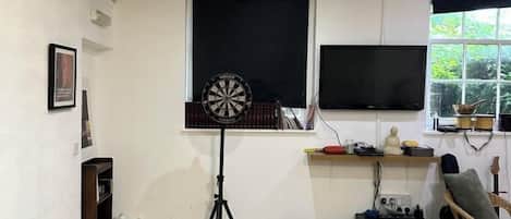 Una habitación con dardos, televisión, ventana y una guitarra.