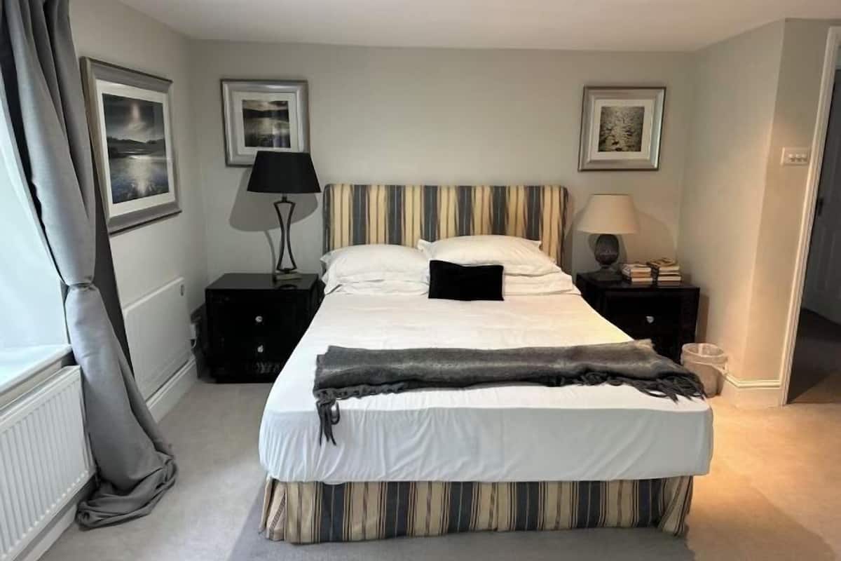A neatly made bed with striped bedding, a bedside table with a lamp, and framed pictures on the wall.