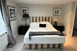 A neatly made bed with striped bedding, a bedside table with a lamp, and framed pictures on the wall. - Huntershields (Northampton)