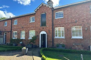 A brick building with a central entrance, multiple windows, and a small garden area with a gravel path. - Huntershields (Northampton)