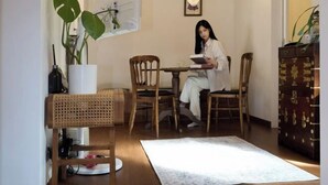 A room with a wooden dining table, two chairs, a white rug, a wooden cabinet, and a potted plant. - Hongdae Hanok (Seoul)