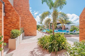 A pool area with lounge chairs, a palm tree, and a brick building.