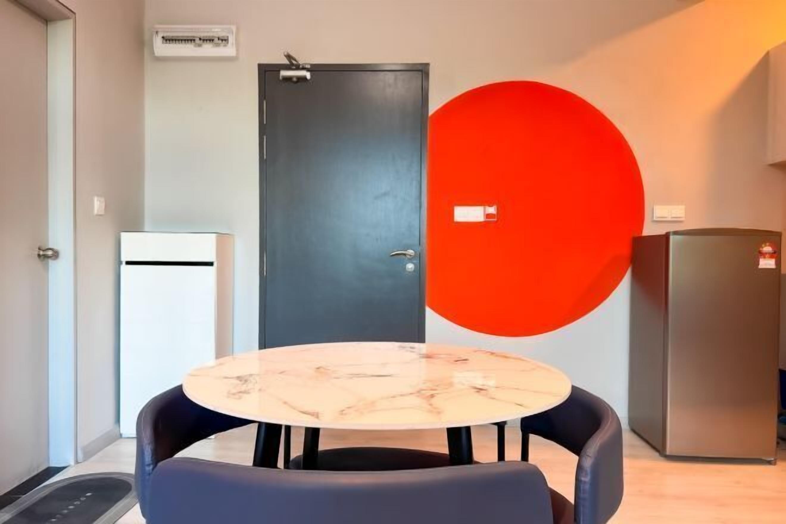 A room with a round table and two chairs, a black door, a red wall feature, and a refrigerator.