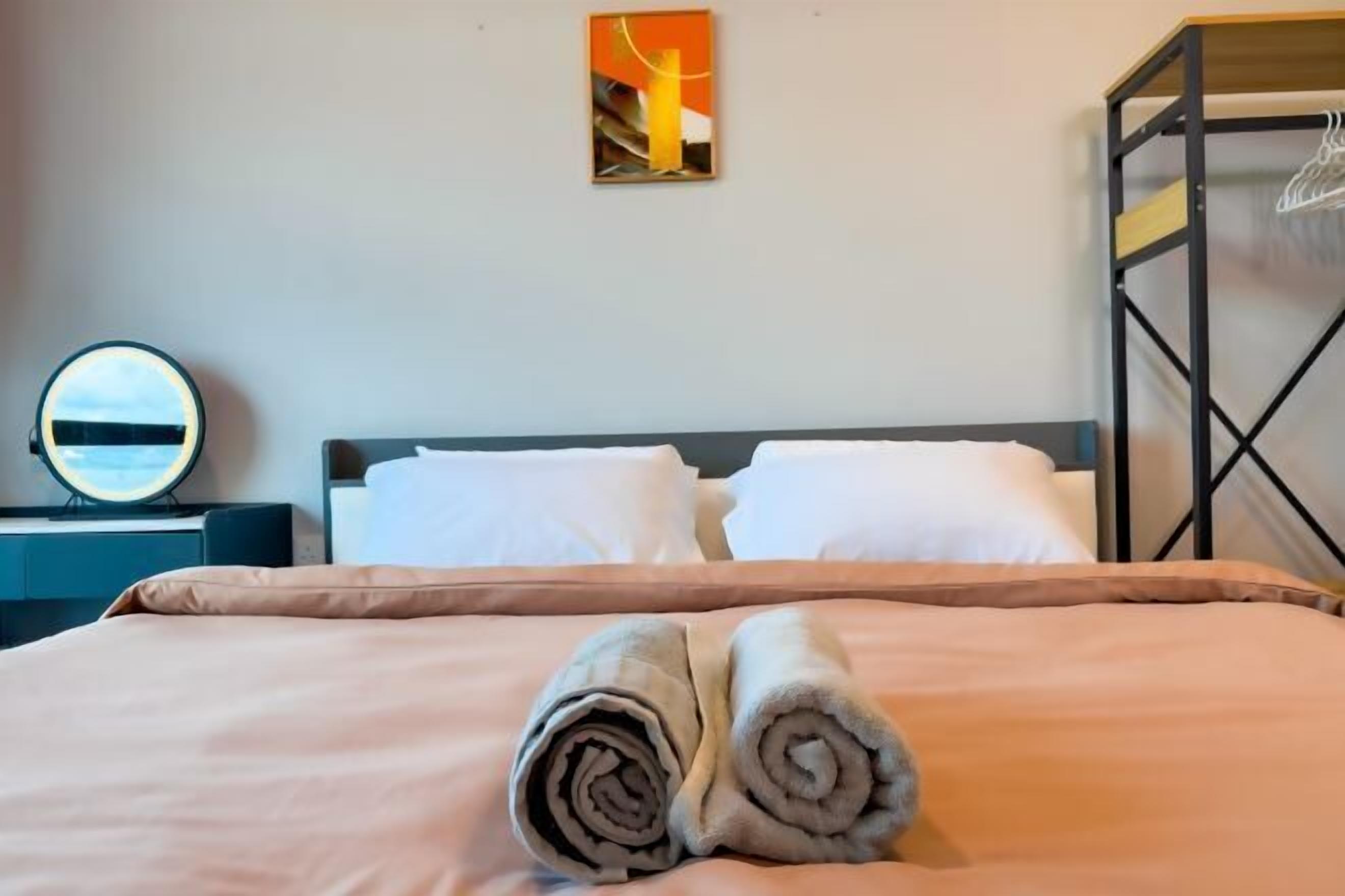 A neatly made bed with a beige bedspread and two rolled towels placed on the bed.