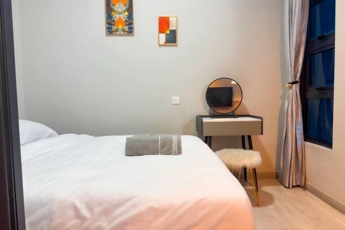 Ein Schlafzimmer mit einem Bett, einem Nachttisch mit Spiegel, einem kleinen Hocker und zwei Bildern an der Wand.