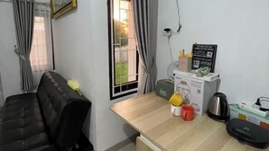 A room with a black leather sofa, a wooden desk with a coffee maker, a kettle, and a signboard. - Breeze House (West Lombok Regency)