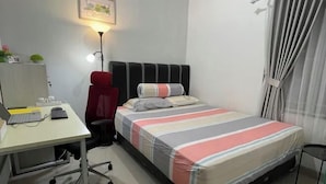 A bedroom with a bed, a desk with a computer, a chair, a lamp, and a window with curtains. - Breeze House (West Lombok Regency)