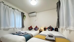 Habitación de hotel con dos camas, ropa de cama blanca, ventilador de techo, unidad de aire acondicionado y una ventana con cortinas.