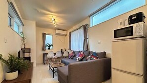 Un espacio habitable compacto con sofá, una pequeña mesa de comedor, microondas y refrigerador.