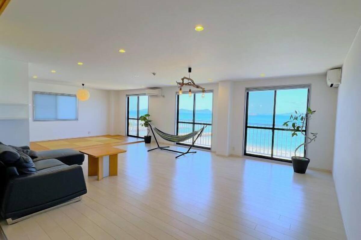 A spacious living area with a sofa, a dining table, a hammock, and large windows with a view of the sea.
