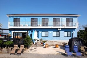 Een gebouw met twee verdiepingen, een balkon, terrasmeubilair en een decoratie van een surfboard.