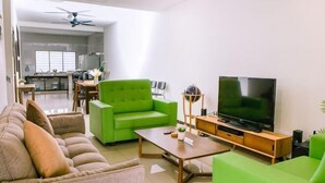 Ein Wohnzimmer mit Sofa, Couchtisch, Fernseher und einem Essbereich im Hintergrund.